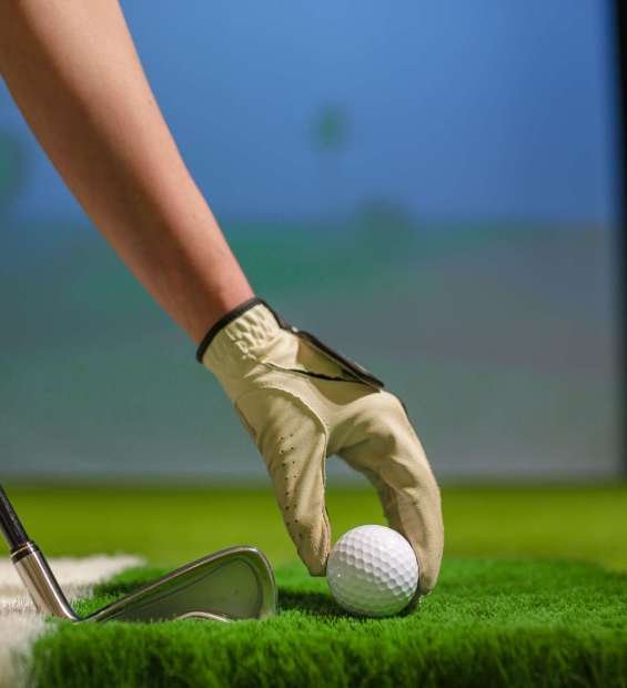 Golfer hand with glove places ball on artificial grass in modern indoor golf simulator during training or practice session